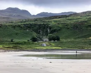 Weiter Strand vor grünen Hügeln und Häusern auf der Isle of Eigg