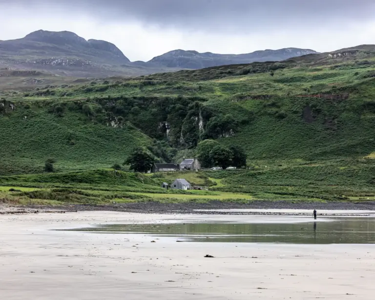 Weiter Strand vor grünen Hügeln und Häusern auf der Isle of Eigg