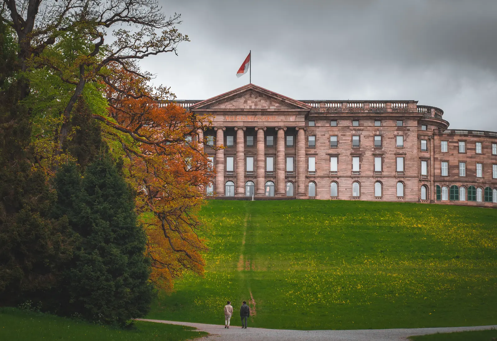 Schloss Wilhelmshöhe hinter einer Wiese und herbstlich gefärbten Bäumen im Bergpark Kassel