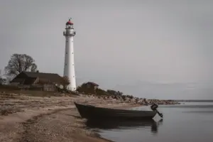 Der weiße Kihnu-Leuchtturm steht neben einem kleinen Boot an der ruhigen estnischen Ostseeküste