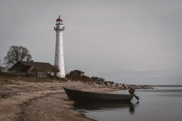 Der weiße Kihnu-Leuchtturm steht neben einem kleinen Boot an der ruhigen estnischen Ostseeküste