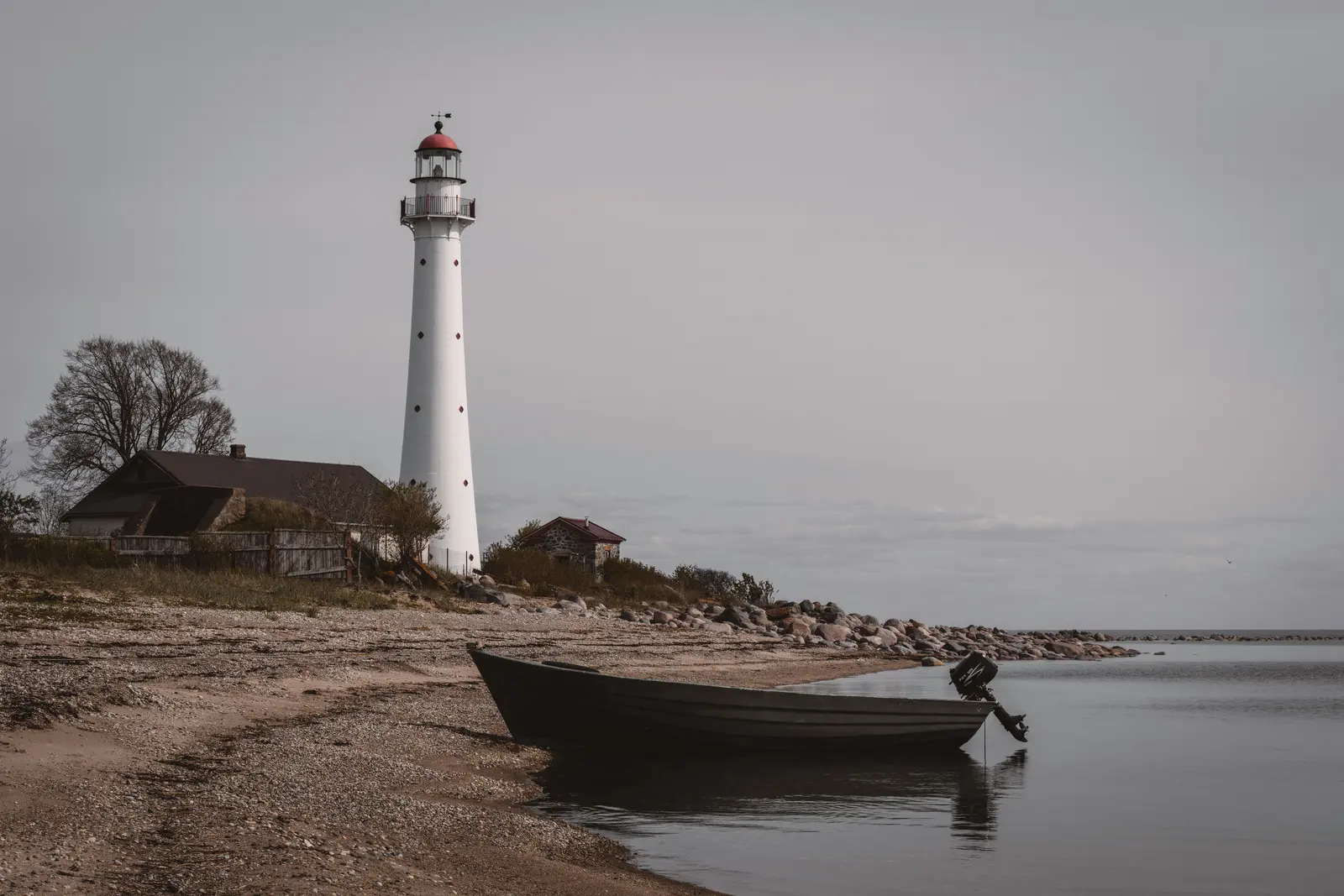 Der weiße Kihnu-Leuchtturm steht neben einem kleinen Boot an der ruhigen estnischen Ostseeküste