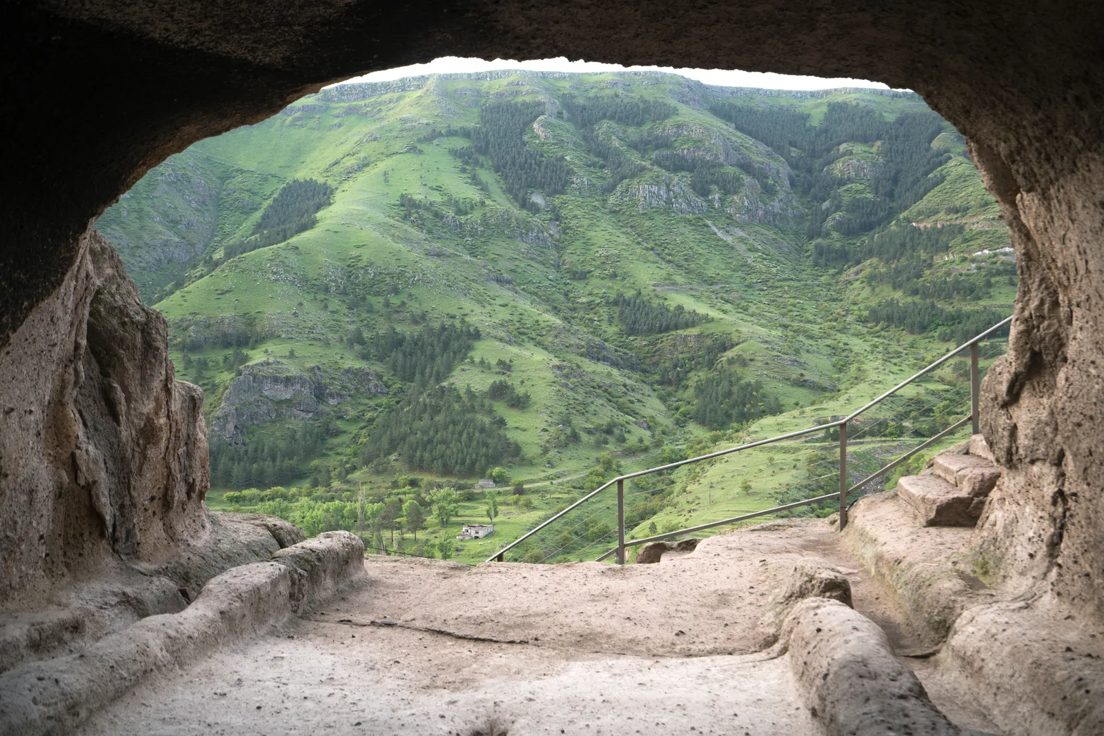 Blick aus einer Vardzia-Höhle über den gesicherten Felsenweg und die grünen Hänge im Mtkvari-Tal